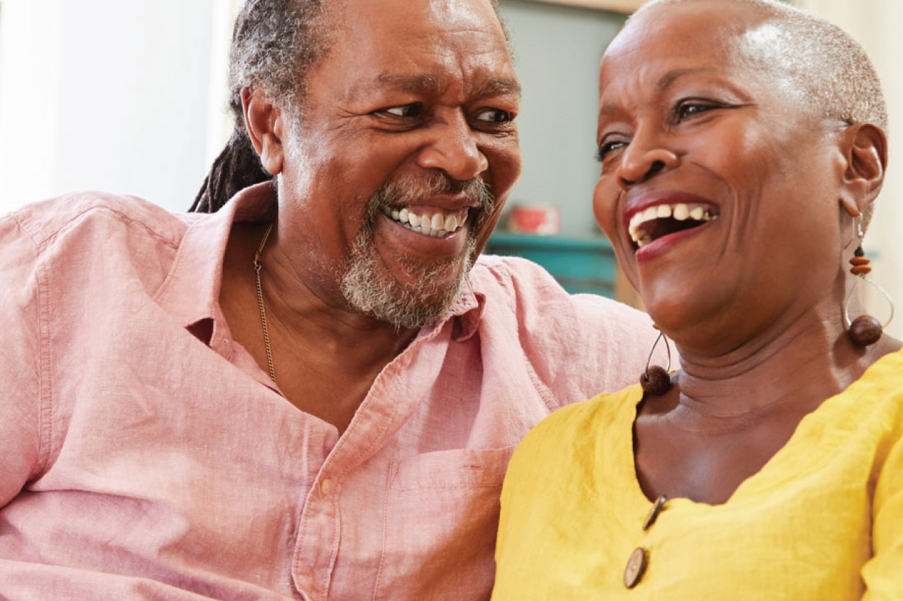 Smiling Senior Couple Sitting On Sofa At Home Together